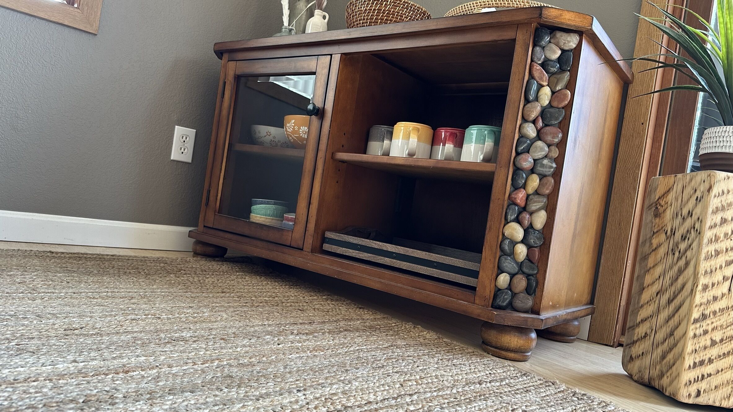 A wooden cabinet with glass doors, a woven rug, and a plant.