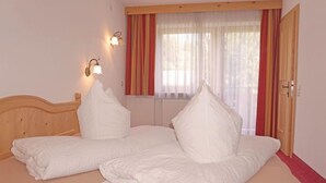 Ein Doppelbett mit zwei Kissen, einem Holzkopfstück, einem Fenster mit Vorhängen und einer Wandleuchte.