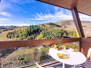 Ein Balkon mit einem Frühstückstisch, der auf eine hügelige Landschaft mit Bäumen und fernen Bergen blickt.