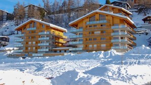Ein mehrstöckiges Holzgebäude mit Balkonen, umgeben von Schnee und Bäumen.