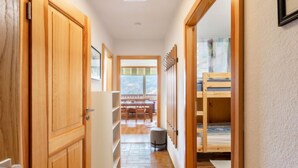 Un pasillo estrecho con puertas de madera, suelo de baldosas y una cama litera al fondo.