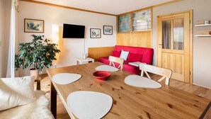 Una habitación acogedora con una mesa de comedor de madera, un sofá rojo y un televisor montado en la pared.