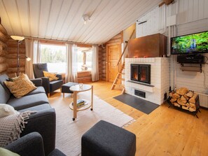A cozy log cabin interior with a fireplace, a sofa set, and a television.