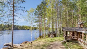 A cabin with a dock and a small shed by a lake surrounded by trees.