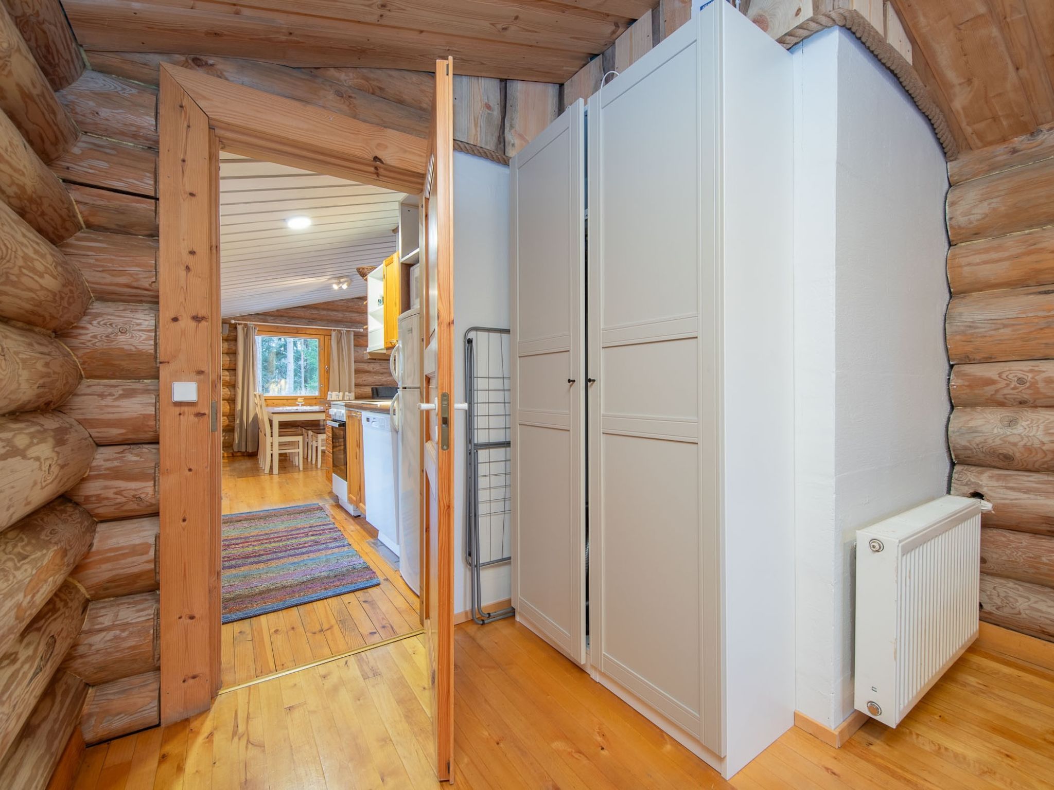 A log cabin interior with a wooden floor, a kitchen area with a refrigerator, and a dining table.