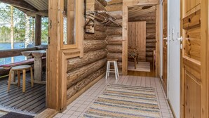 A log cabin with a wooden deck, a small table and chairs, a bench, and a window overlooking a natural landscape.