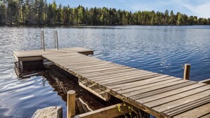 Un muelle de madera se extiende sobre un lago tranquilo, rodeado de un denso bosque.