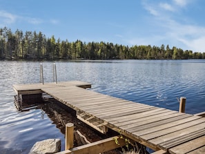 Un muelle de madera se extiende sobre un lago tranquilo, rodeado de un denso bosque.