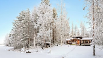 Una cabaña rodeada de árboles cubiertos de nieve, con cielo despejado.