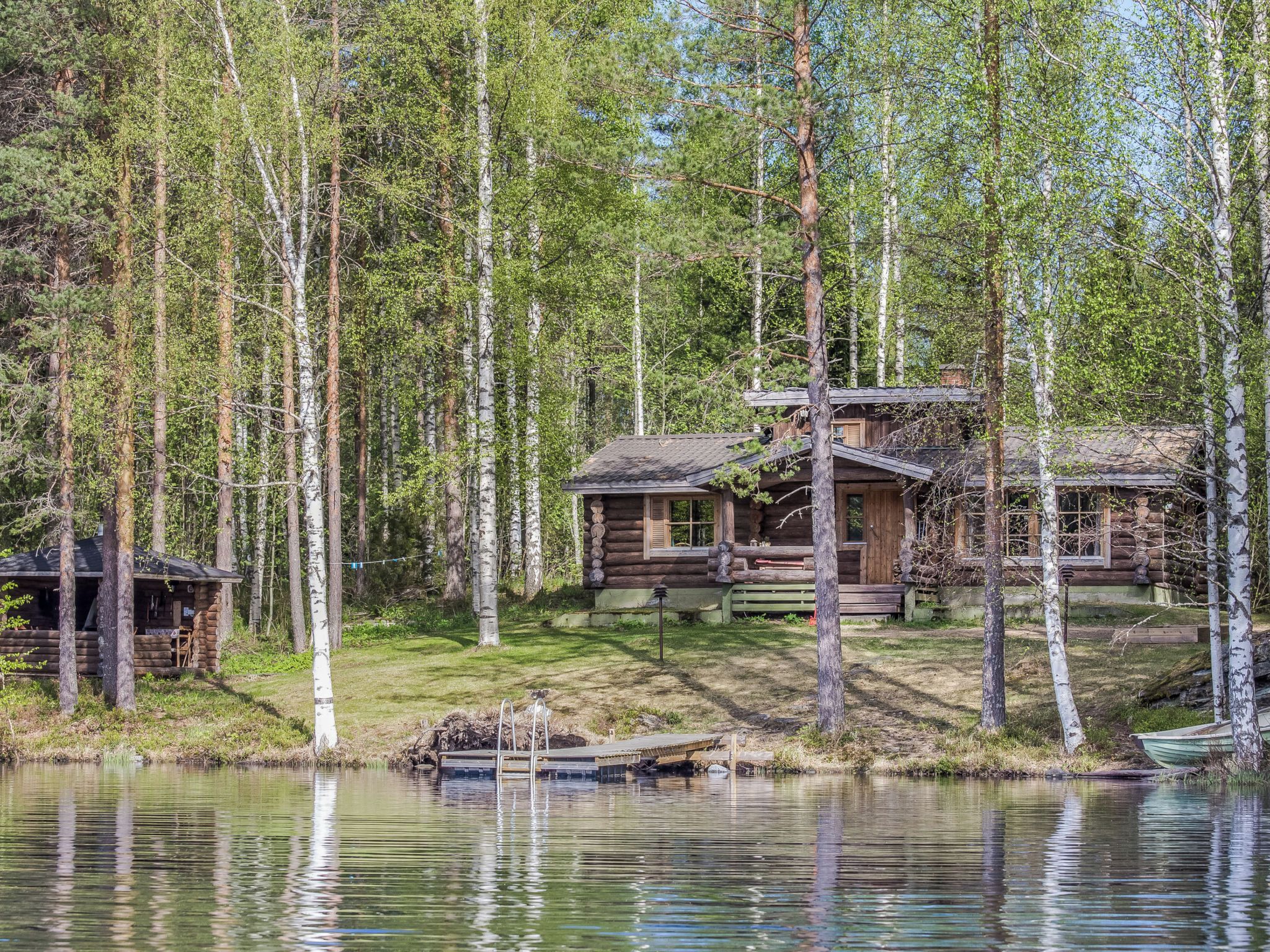 Une cabane avec un quai s’avançant dans un lac, entourée d’une forêt.