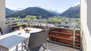 Varanda com mesa e cadeiras, com vista para uma paisagem montanhosa e edifícios no vale.
