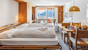 Quarto de hotel com duas camas, um espaço para refeições e vista para montanhas.