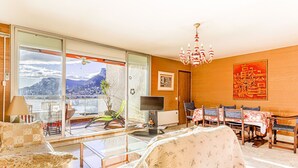 Een ruime woonkamer met een grote schuifpui die uitkomt op een balkon, een eethoek met tafel en stoelen, en een televisie op een dressoir.