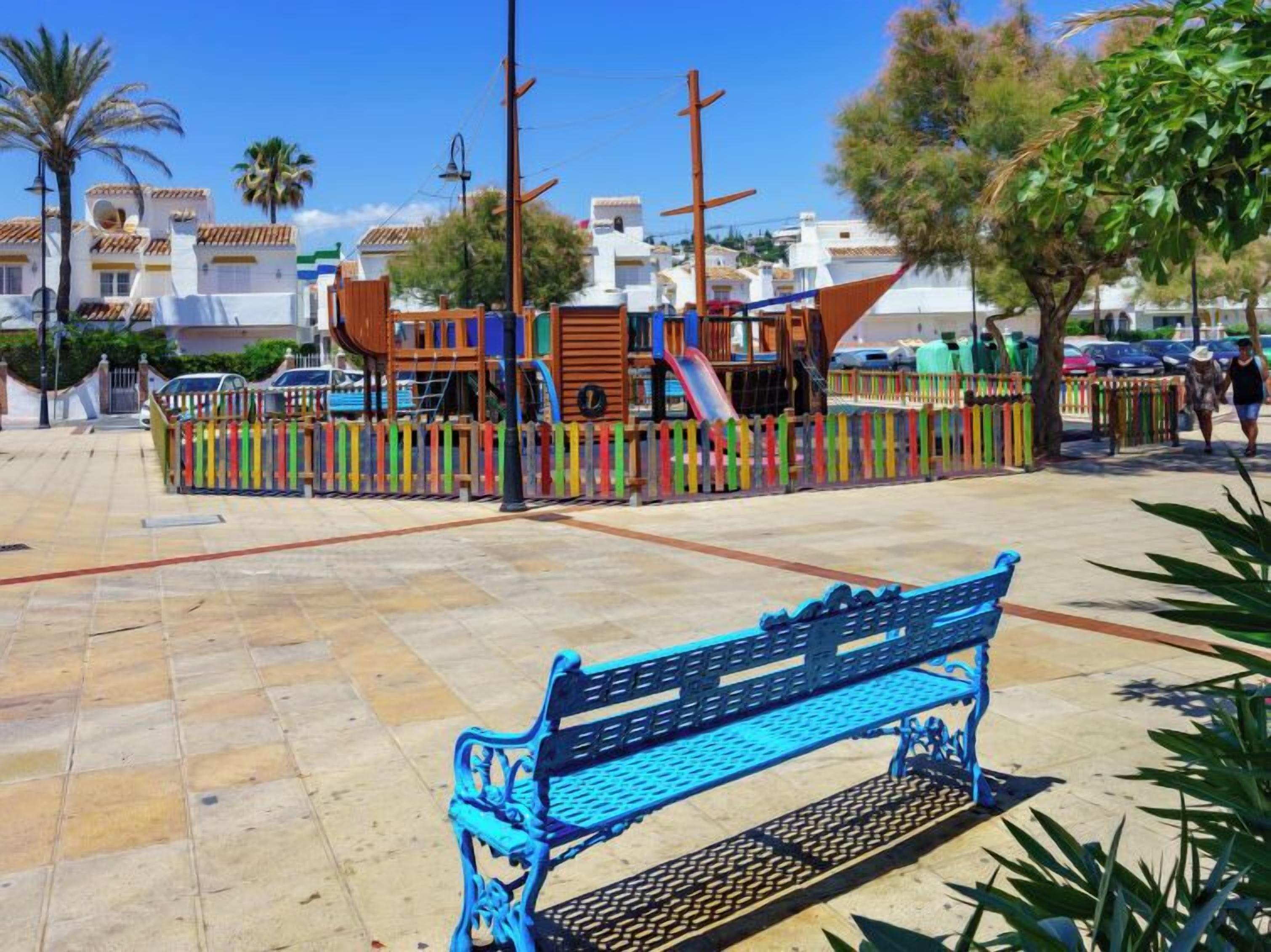 A playground with a slide and climbing structures, surrounded by a colorful fence.