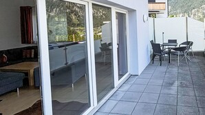 Un salon moderne comprenant un canapé, une table basse et une porte vitrée donnant sur un balcon équipé d’un ensemble de mobilier de salle à manger.