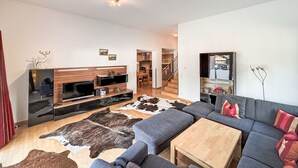 Un salon moderne avec un canapé gris, une table basse en bois et un grand téléviseur à écran plat.