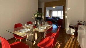 Un comedor con una mesa de vidrio y sillas rojas, un florero con flores y vistas a una sala de estar con un sofá y una ventana.