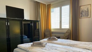 Habitación de hotel con dos camas, un televisor en un mueble y una ventana con cortinas.