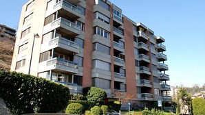 Un edificio residencial de varios pisos con balcones, cielo despejado y un letrero de estacionamiento.