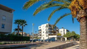 A modern apartment building with balconies, a paved walkway, and palm trees. - Rive Gauche by Interhome (Fréjus)