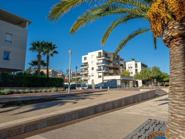 A modern apartment building with balconies, a paved walkway, and palm trees.