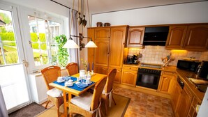 Une cuisine avec des meubles en bois, une table à manger dressée avec de l’assiette bleue et blanche, et une vue sur un jardin par la fenêtre.