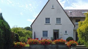 Une maison à deux étages, avec un toit triangulaire, une petite fenêtre à l’étage supérieur et une porte au rez-de-chaussée.