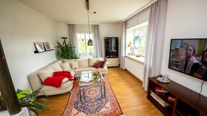 Un salon moderne avec un canapé beige, une table basse, un téléviseur et une grande fenêtre avec des rideaux.