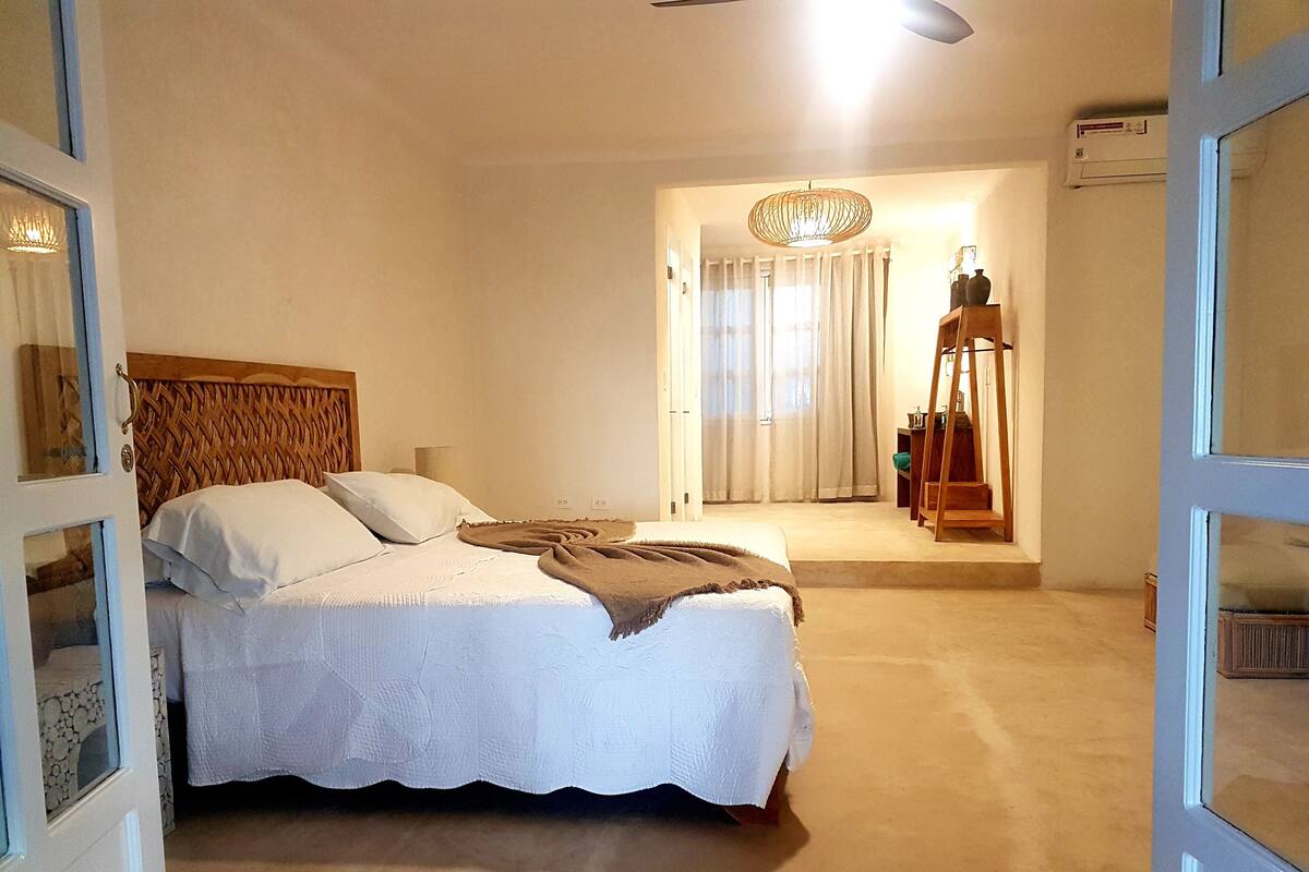 Un dormitorio con cama, cabecera de madera, lámpara de pie y vista a un pasillo con escalera.