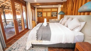 A spacious bedroom with a large bed, wooden walls, and a view through a glass door to an outdoor area. - Amaité Beach Hotel (Isla Holbox)