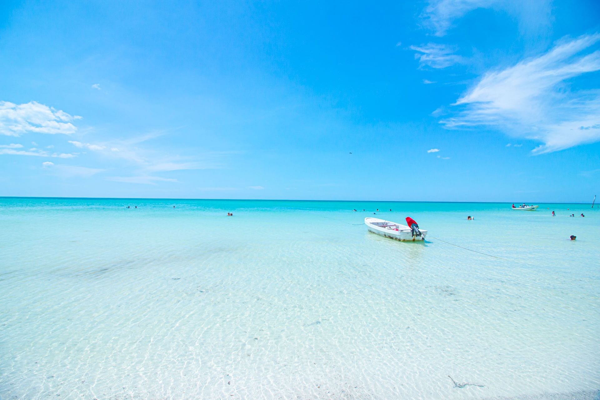 A boat tied to a dock on a clear turquoise beach with shallow water.