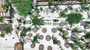 An aerial view of a resort with thatched-roof structures, palm trees, and circular seating areas. - Amaité Beach Hotel (Isla Holbox)