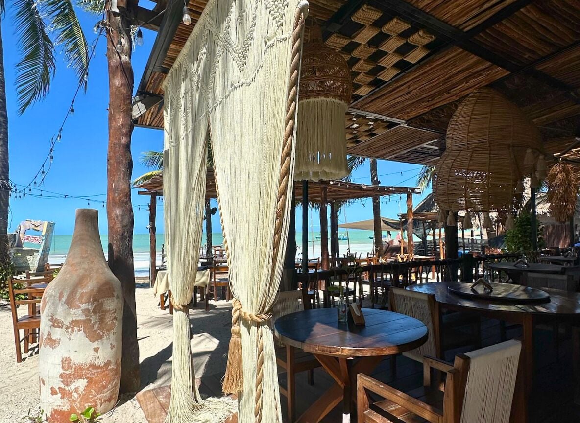 An outdoor seating area with wooden tables and chairs, a large decorative vase, and a thatched roof structure.