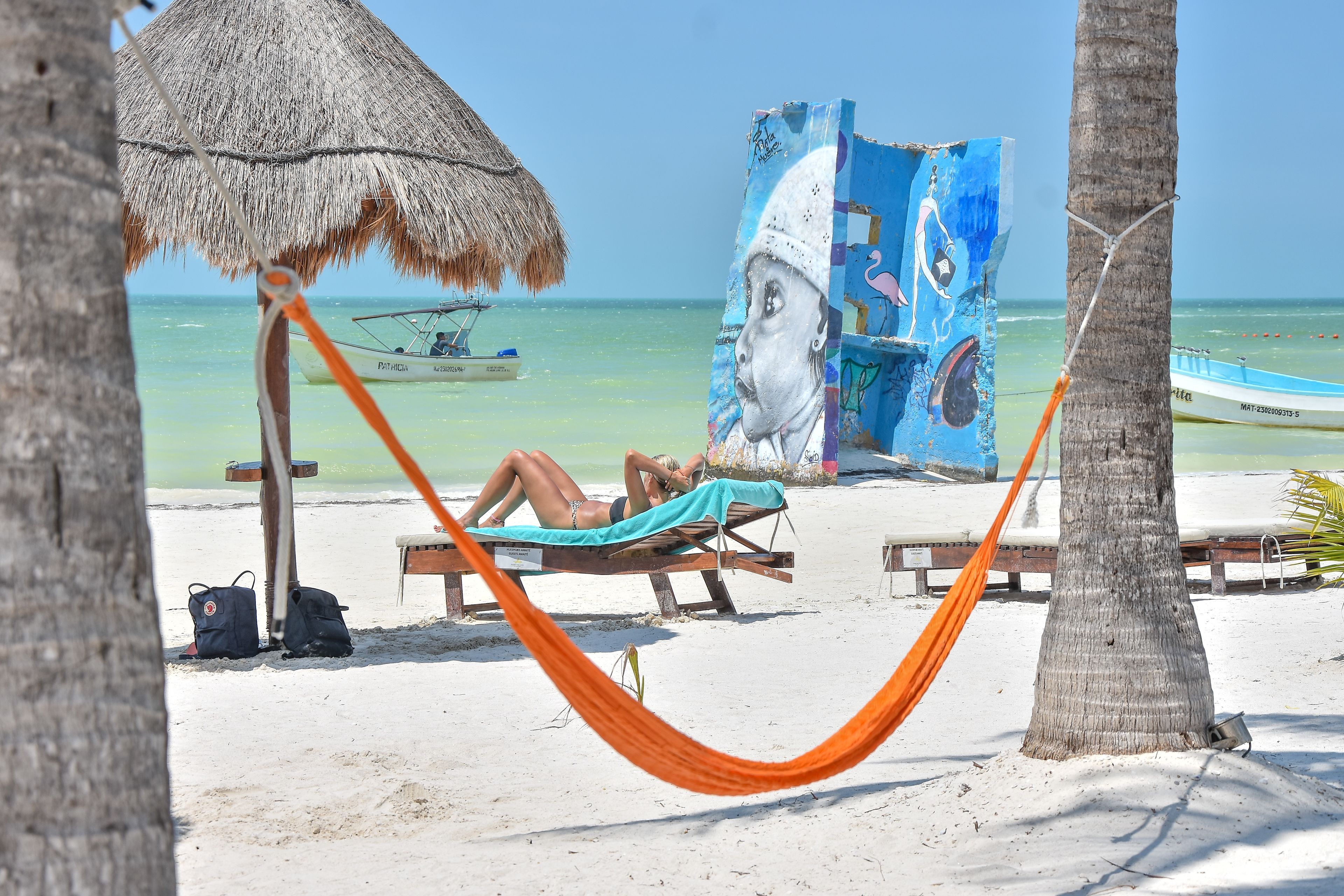 A beach scene with a hammock, a thatched umbrella, and a mural on a wooden structure.