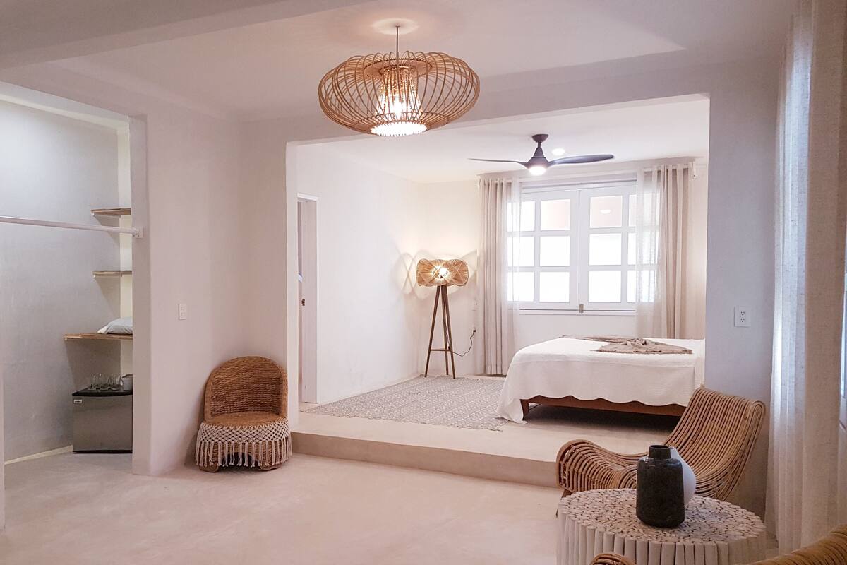 Un dormitorio amplio con una cama grande, un ventilador de techo, una lámpara de pie y vistas a un balcón.