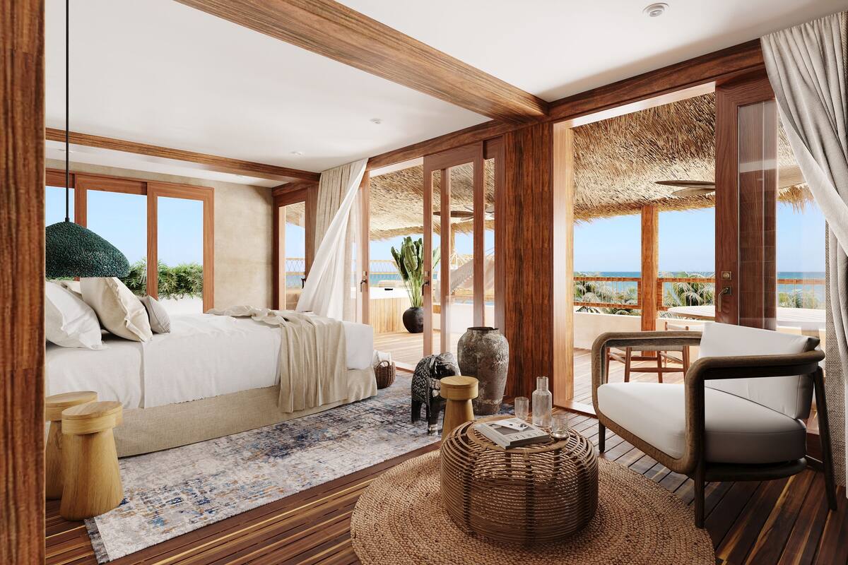 Un dormitorio con cama, una silla, una mesita y vista al océano.