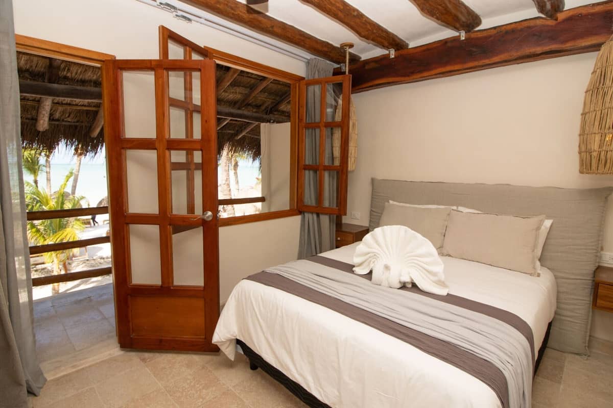 Un dormitorio con una cama, una ventana que ofrece vistas a palmeras y una puerta de madera.