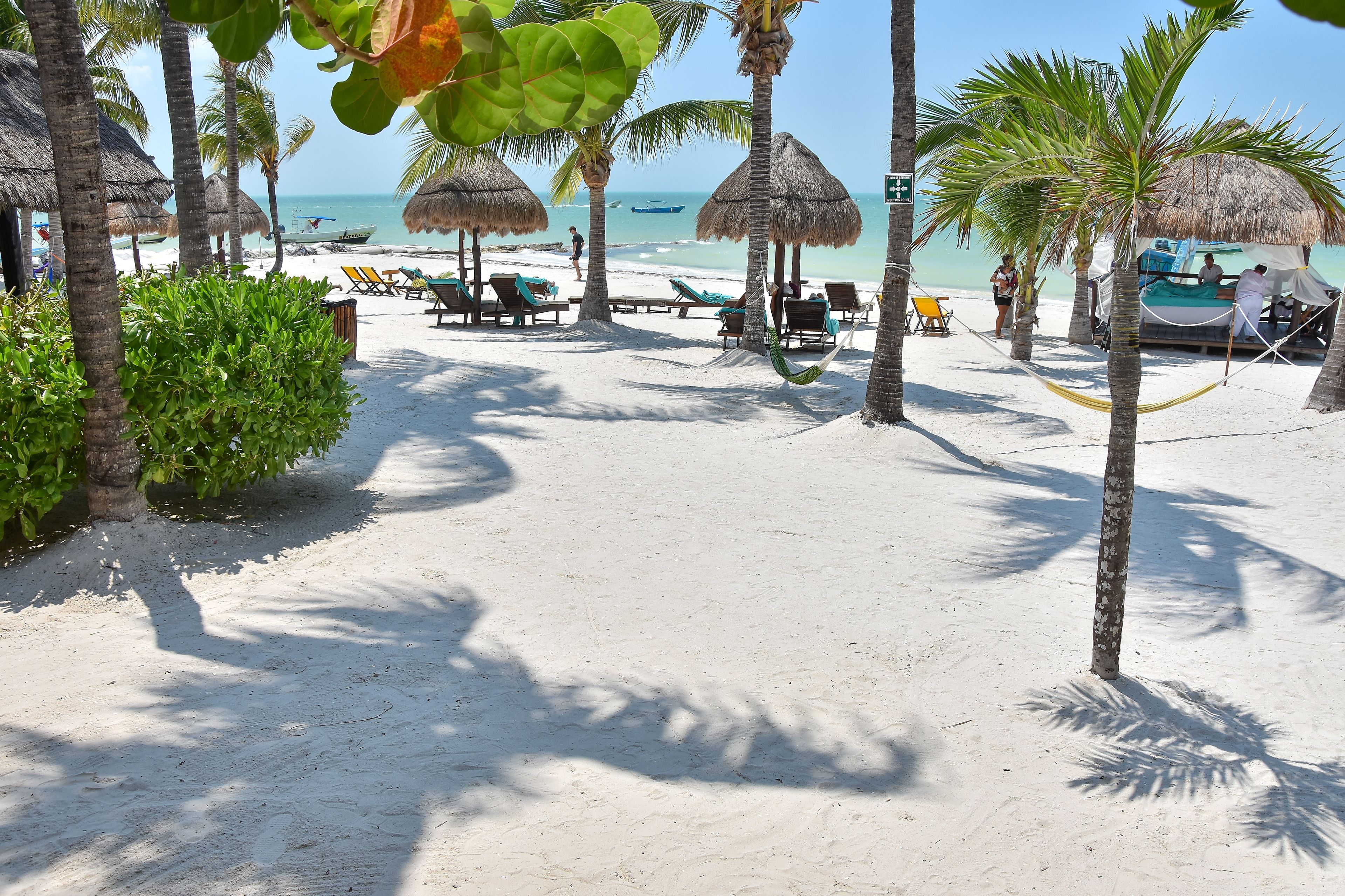 A beach with thatched umbrellas, lounge chairs, and a boat.