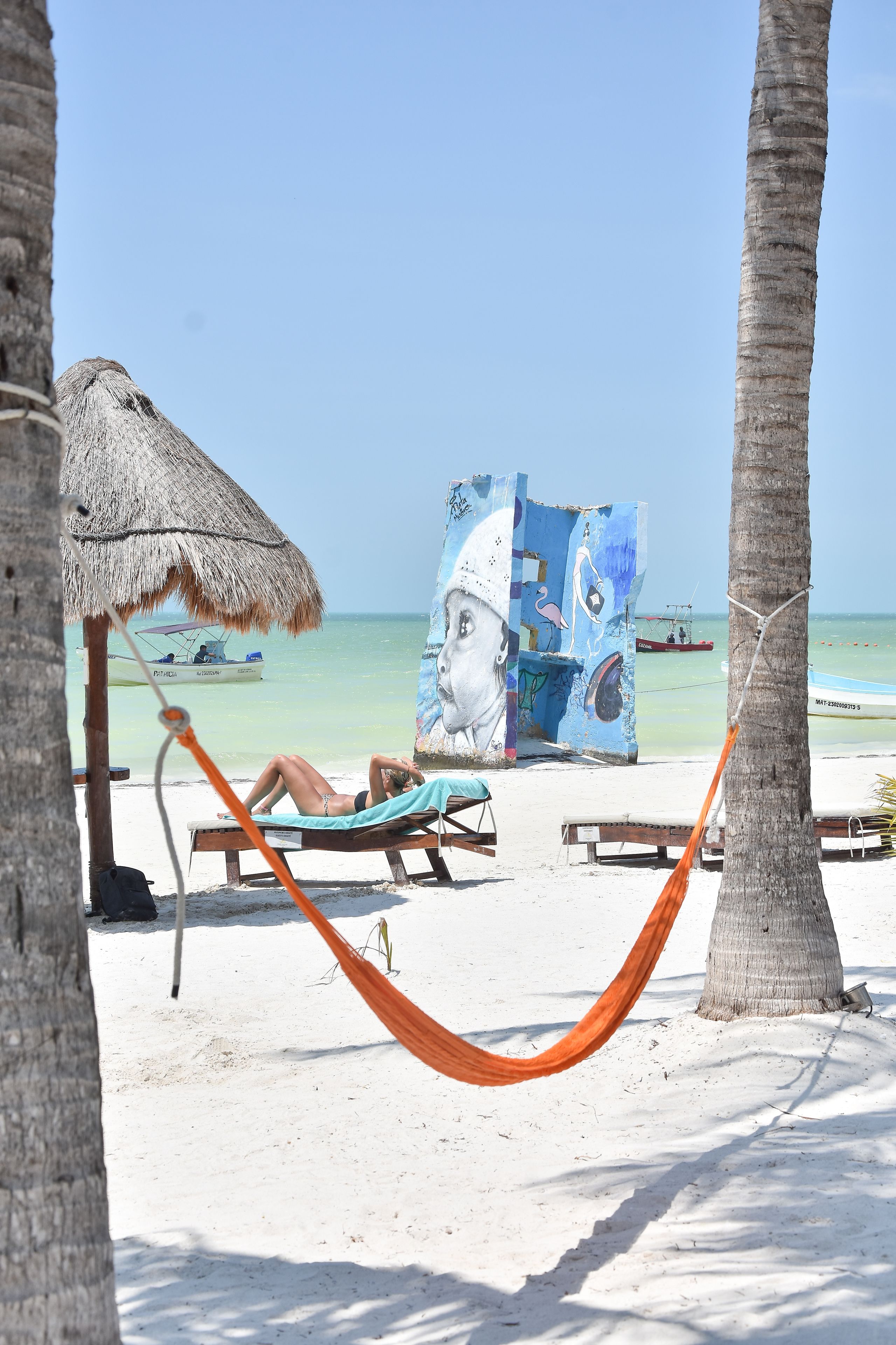 A beach scene with a hammock, a thatched umbrella, and a large abstract painting.