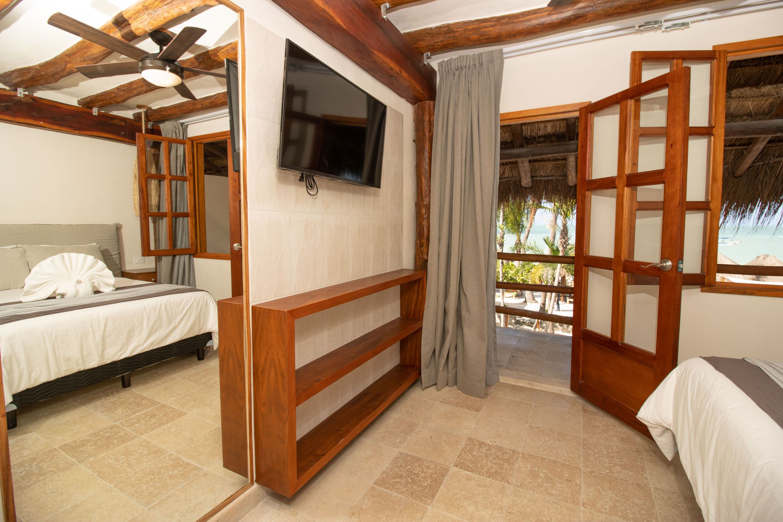 Une chambre d’hôtel avec un lit, une télévision, une étagère en bois et un balcon avec vue.