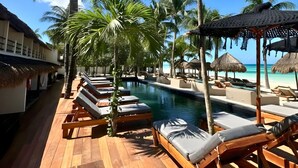 A poolside area with lounge chairs, palm trees, and thatched umbrellas. - Amaité Beach Hotel (Isla Holbox)