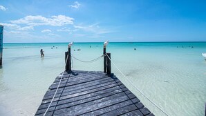 A wooden pier leading to a beach with clear turquoise water and a few people swimming. - Amaité Beach Hotel (Isla Holbox)