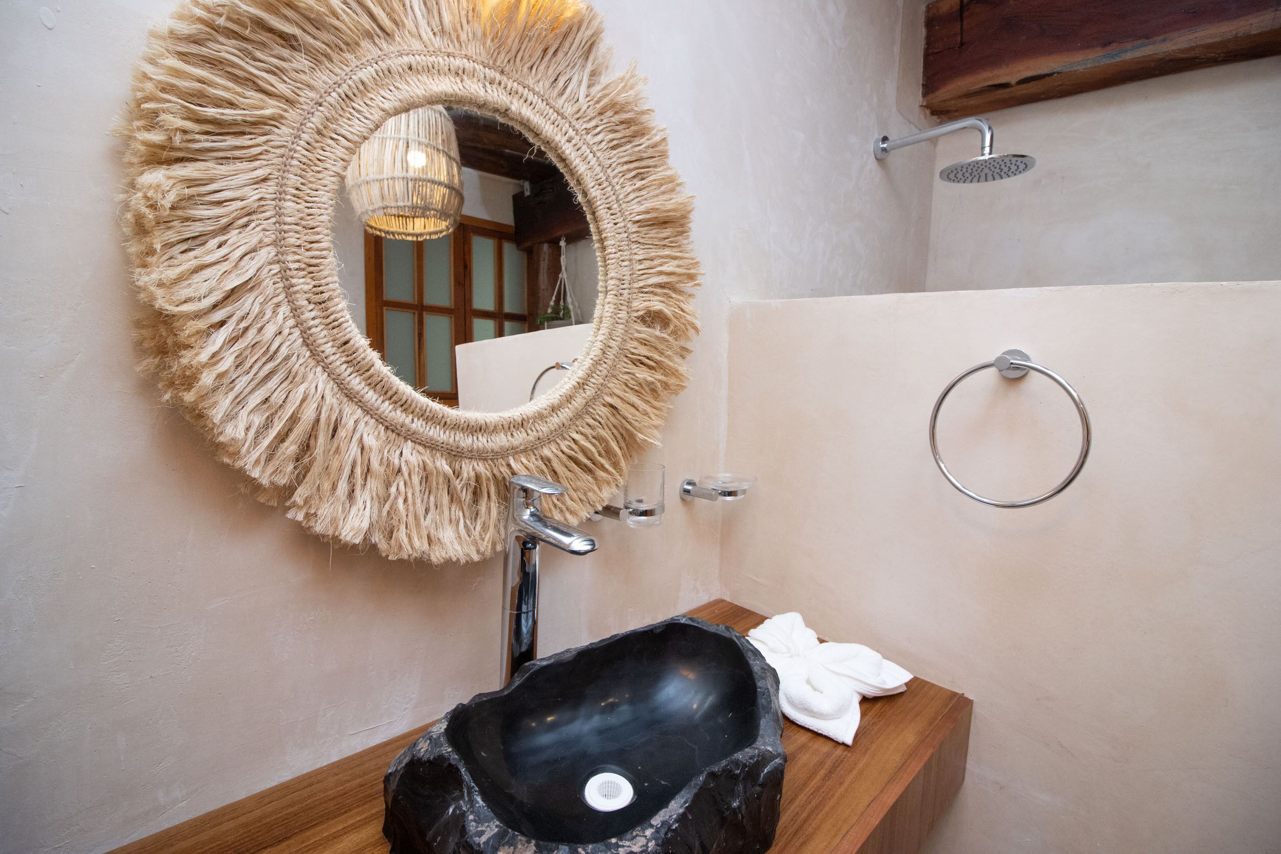 A bathroom with a round mirror, a black sink, a towel, a shower, and a wooden vanity.