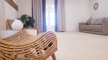 A living room with a wicker chair, a sofa, a potted plant, and a window with curtains.