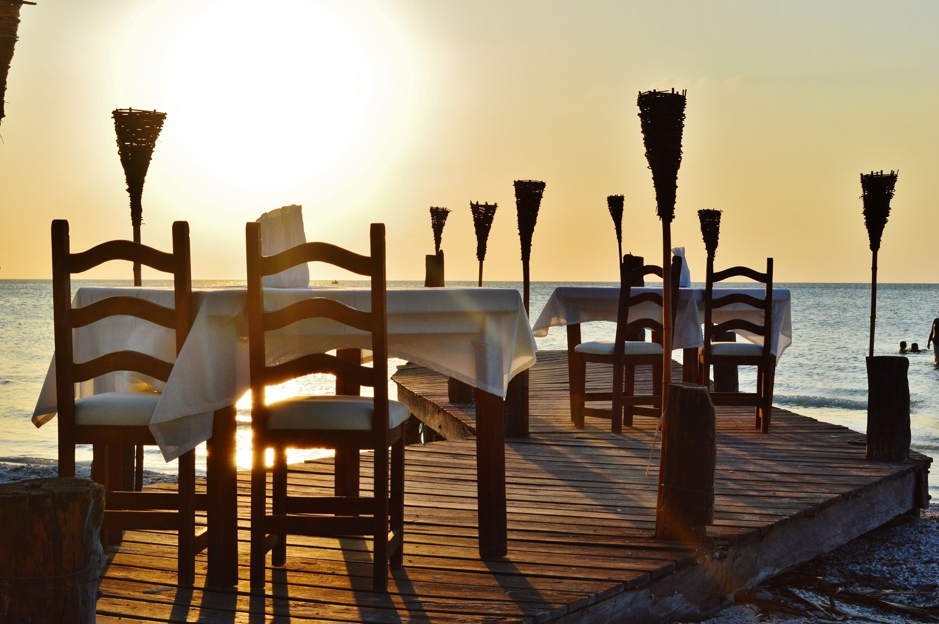 A wooden deck with tables and chairs set up for dining, overlooking the sea.
