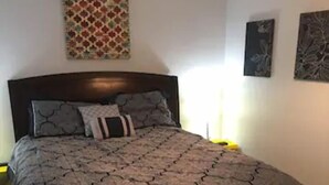 A bed with a patterned bedspread, a headboard, and two wall-mounted artworks. - Private Basement Apartment (Athens)