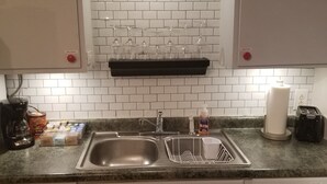 A kitchen with white subway tiles, a double sink, a coffee maker, a toaster, and a dish rack. - Private Basement Apartment (Athens)