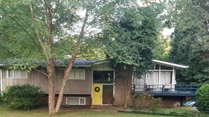 A single-story house with a yellow front door, a covered porch, and a brick foundation. - Private Basement Apartment (Athens)