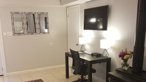 A living room with a black office chair, a small table with two lamps, a TV on the wall, and a fireplace. - Private Basement Apartment (Athens)