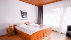 Una cama de madera en una habitación con una mesita de noche, un cuadro enmarcado en la pared y una ventana con cortinas.